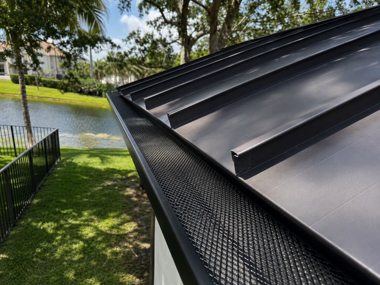 Black gutter guard mesh fitted to a gutter beneath a dark metal roof